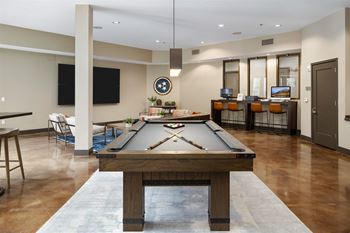 A pool table is in the middle of a room with a TV and a clock on the wall.